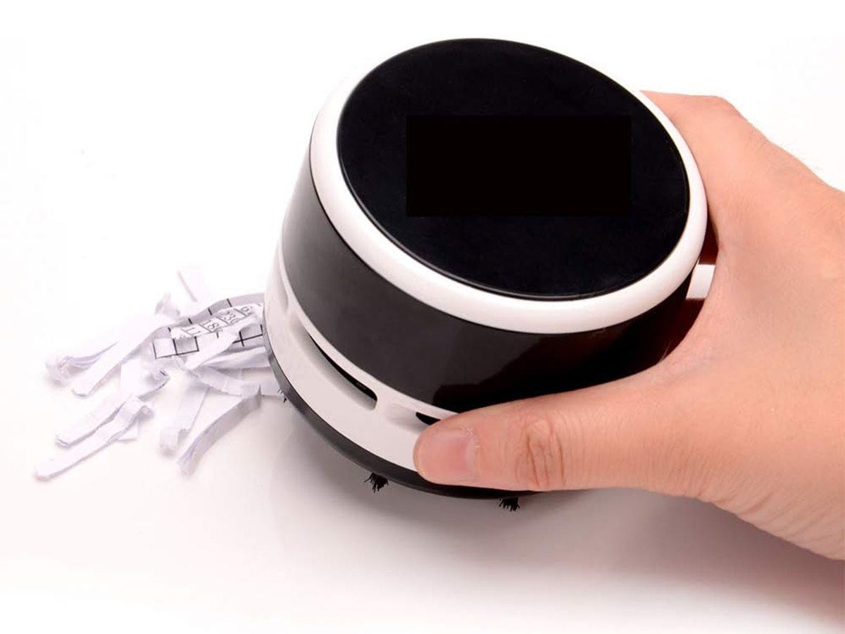 A hand holding a black and white cordless tabletop mini vacuum.