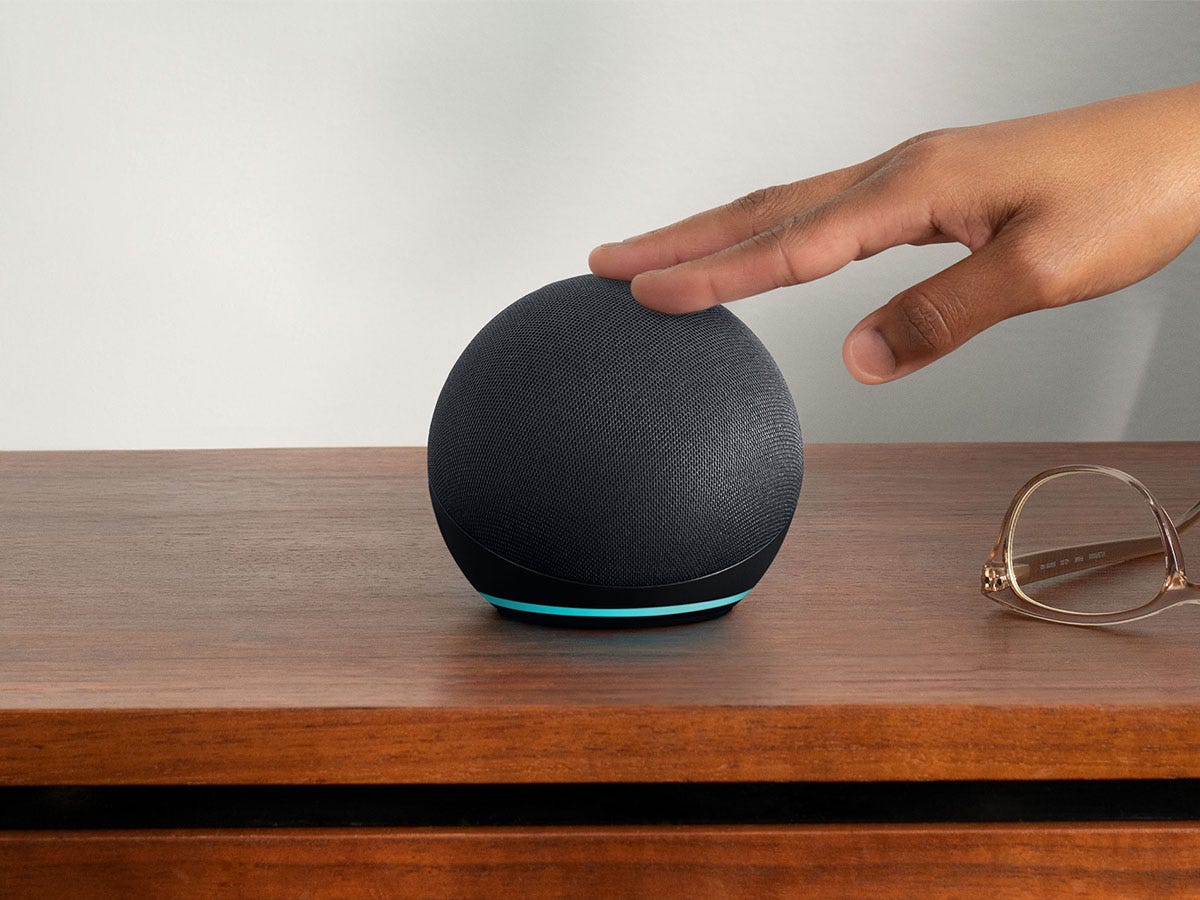 A hand touching the black Amazon Echo Dot 5th Generation on a wooden surface.