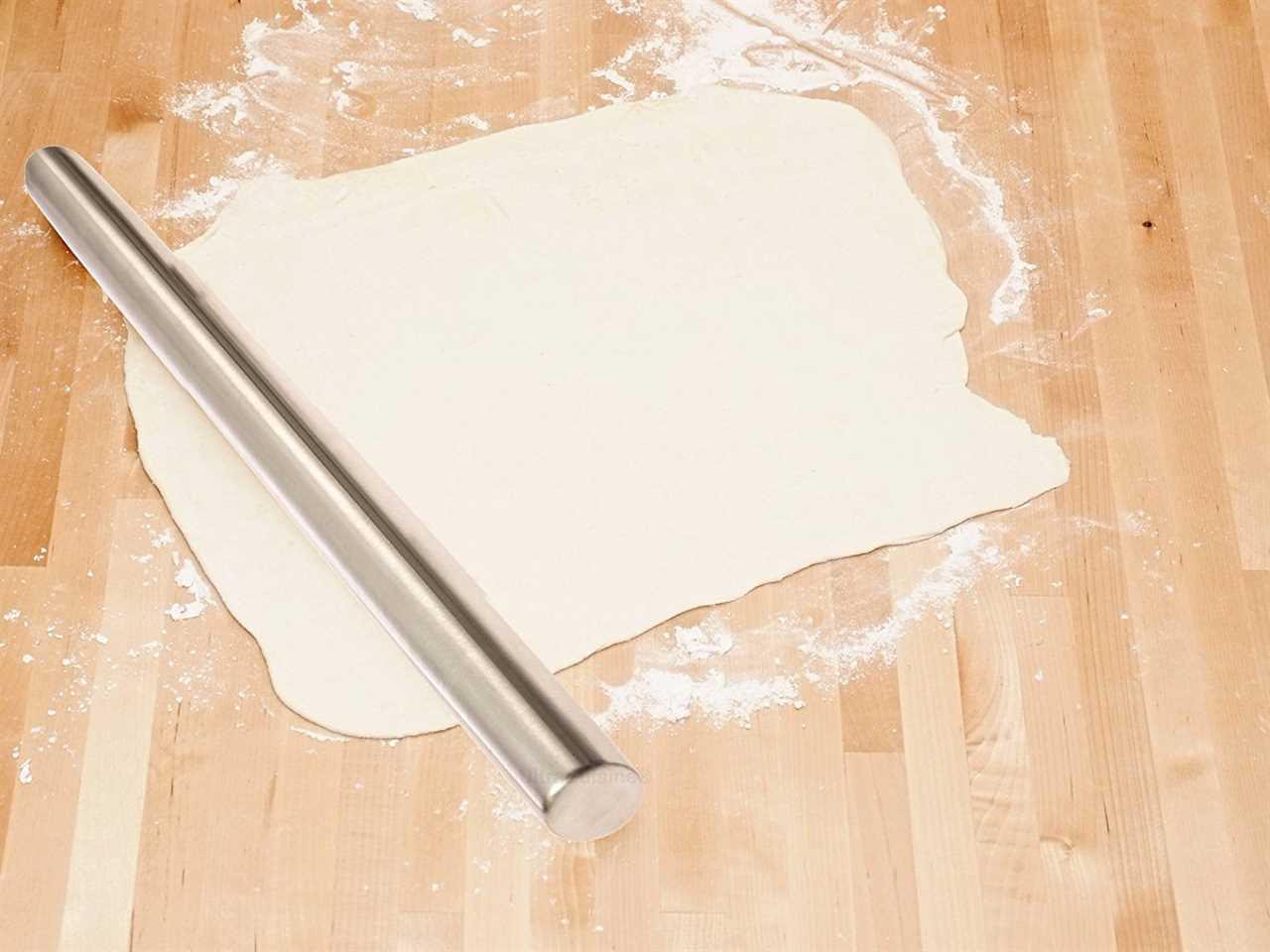 A steel rolling pin on top of a sheet of dough and flour.