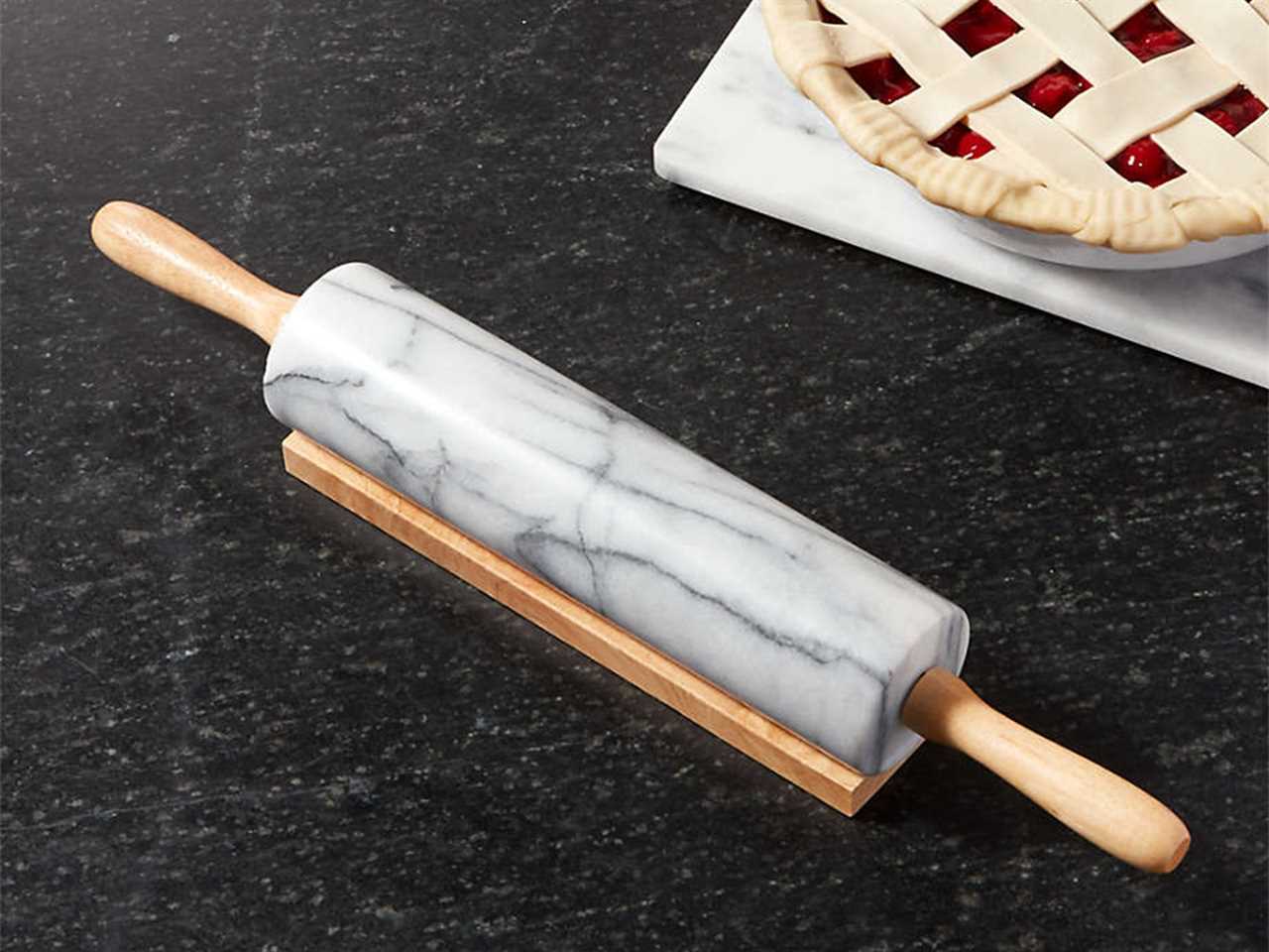 A marble rolling pin with wooden handles on a black countertop next to a pie.