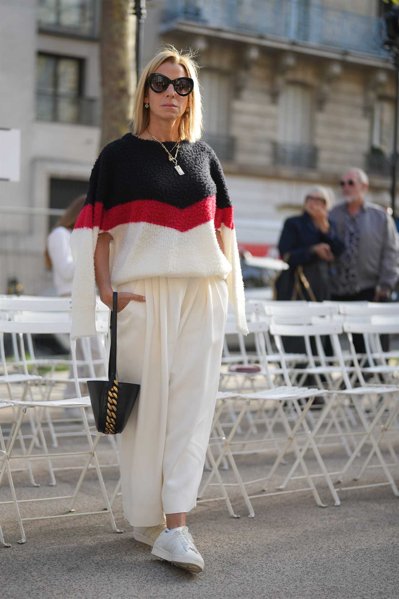 A woman wearing a sweater, white pants and white sneakers with big sunglasses