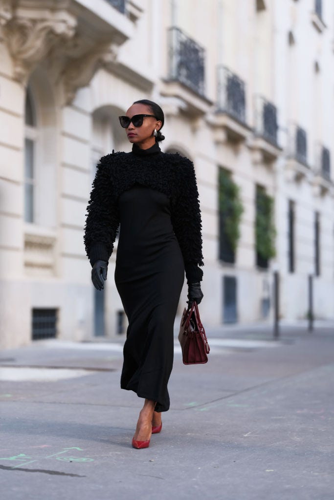 A women walking on the street wearing a black sweater, skirt, sunglasses and gloves with red heels and a red handbag.