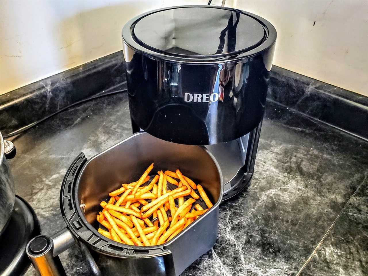 The basket of the Dreo Aircrisp Pro Air Fryer is full of evenly cooked fries and pulled out of the appliance that is sitting on a counter.