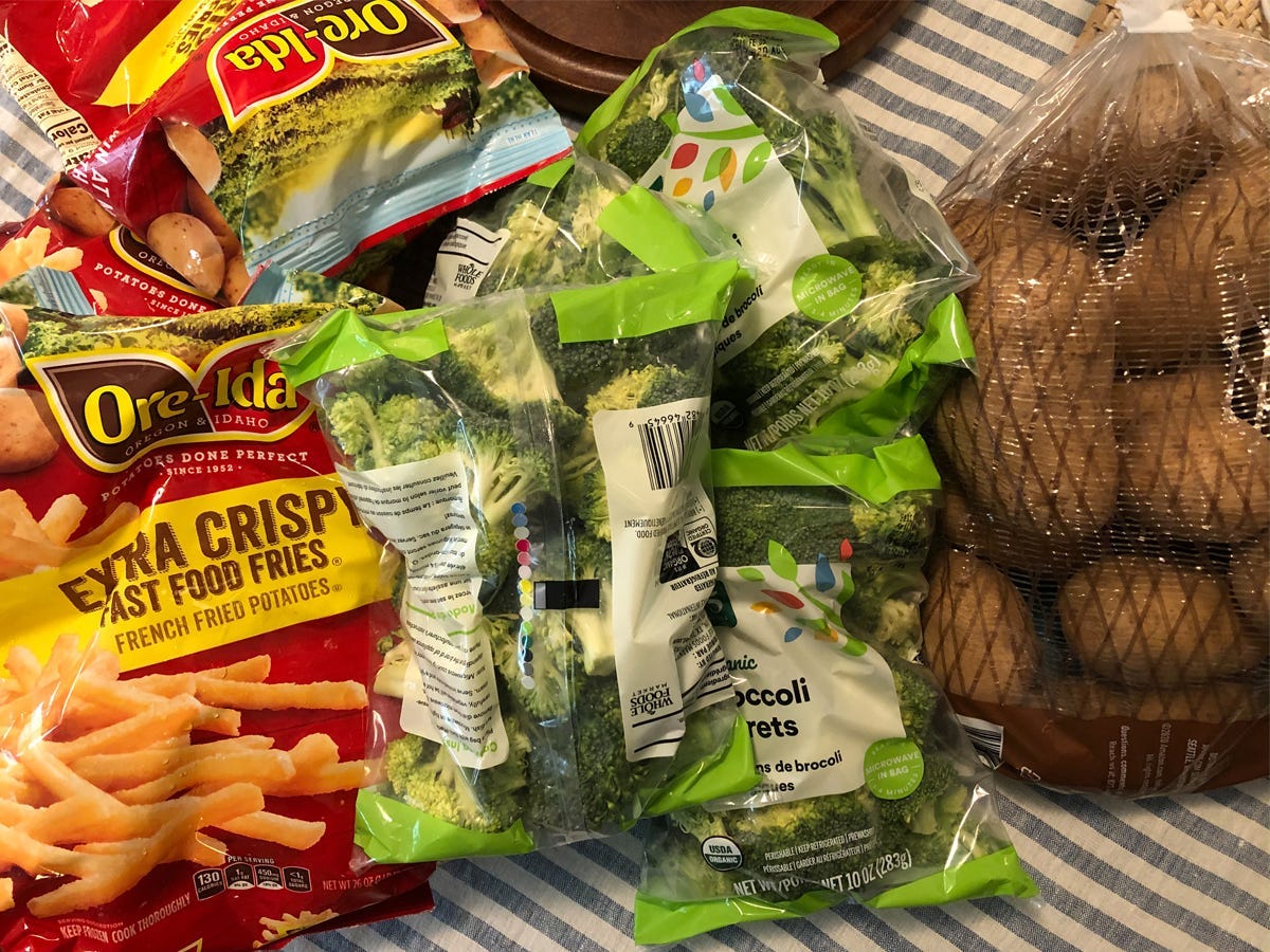 Bags of Ore-Ida Extra Crispy Fast Food Fries, frozen broccoli florets, and raw potatoes piled up.