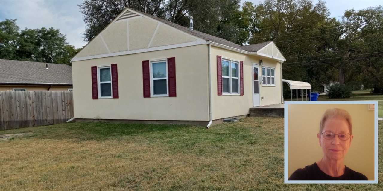 An image of a woman on top of a cream-colored house with red shutters.