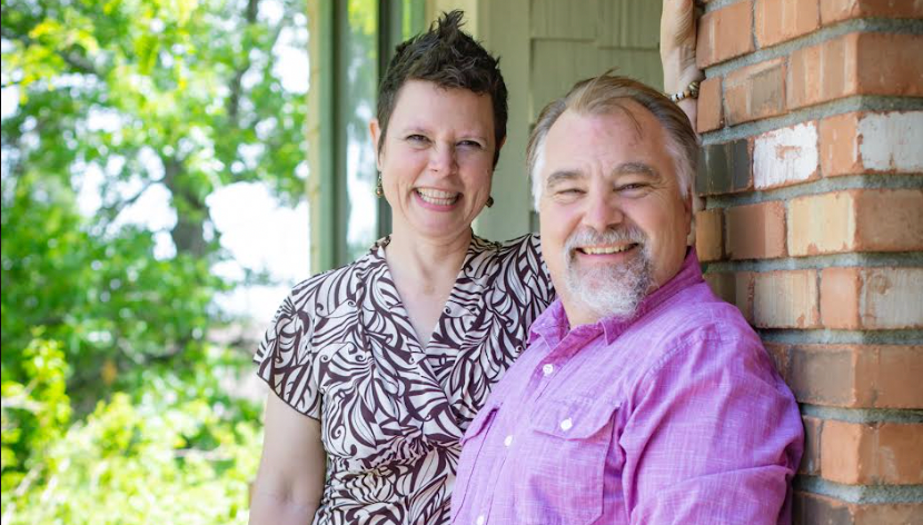 Two people pose in front of a brick wall.