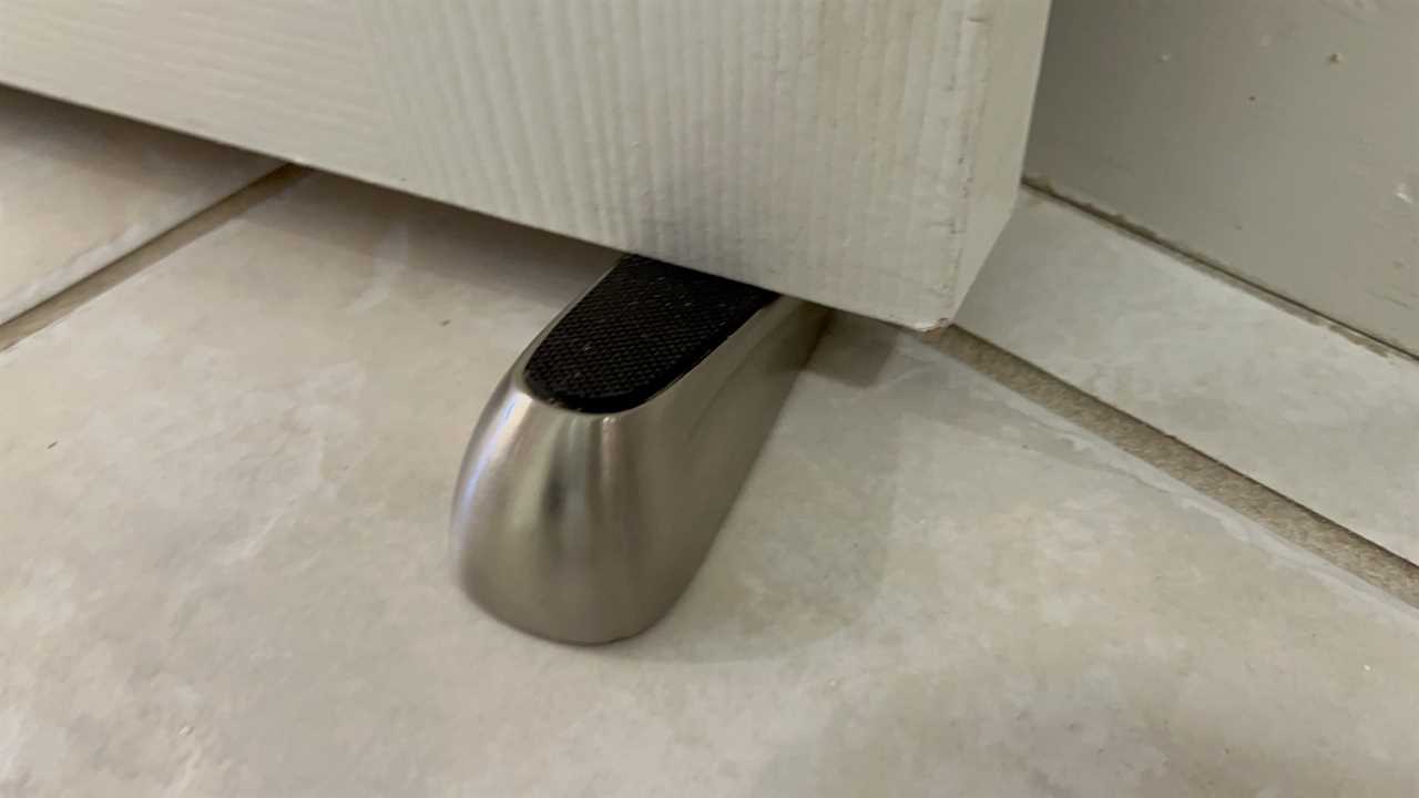 silver doorstop with black textured surface on top wedged under an open door