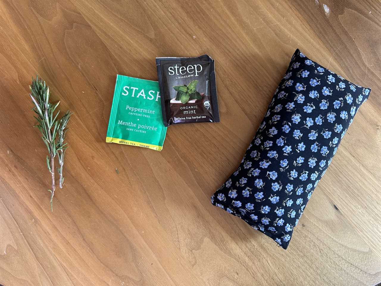 items on wood table sprig of rosemary two packets of mint tea and a black rectangular sack covered in little blue flowers