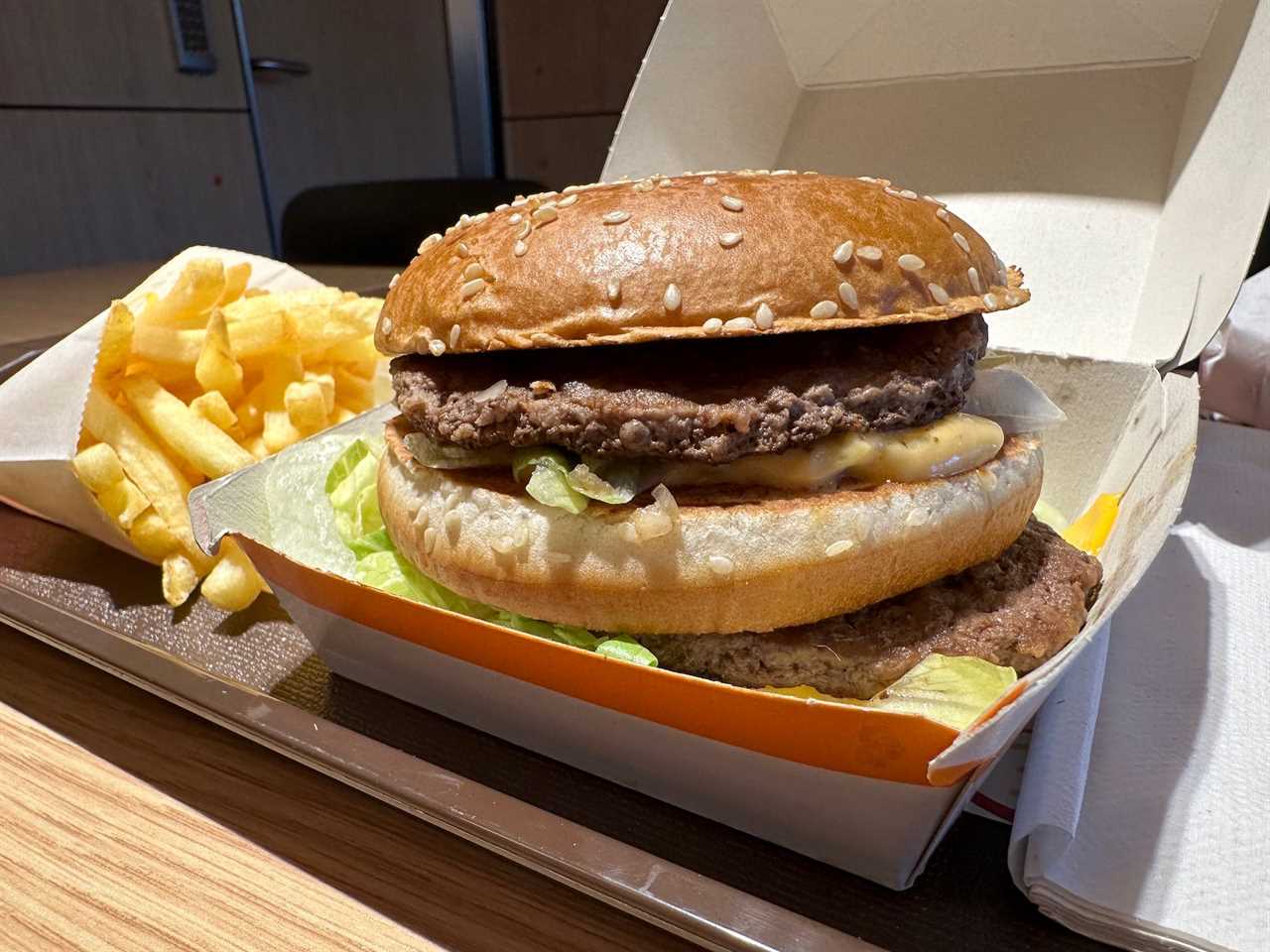 mcdonalds big mac in paper burger box on a well lit table next to french fries