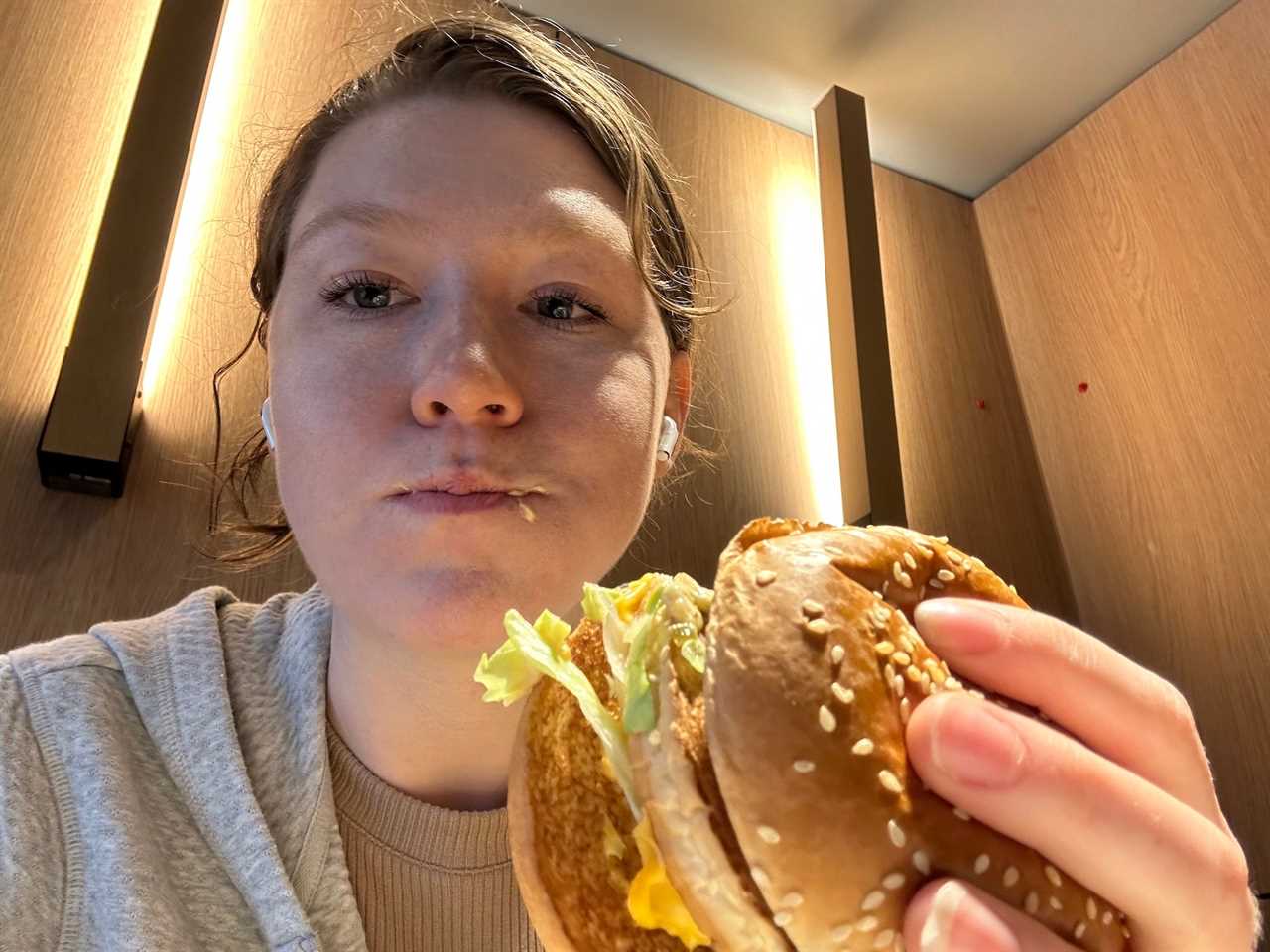 woman selfie eating mcdonalds big mac in front of wood wall