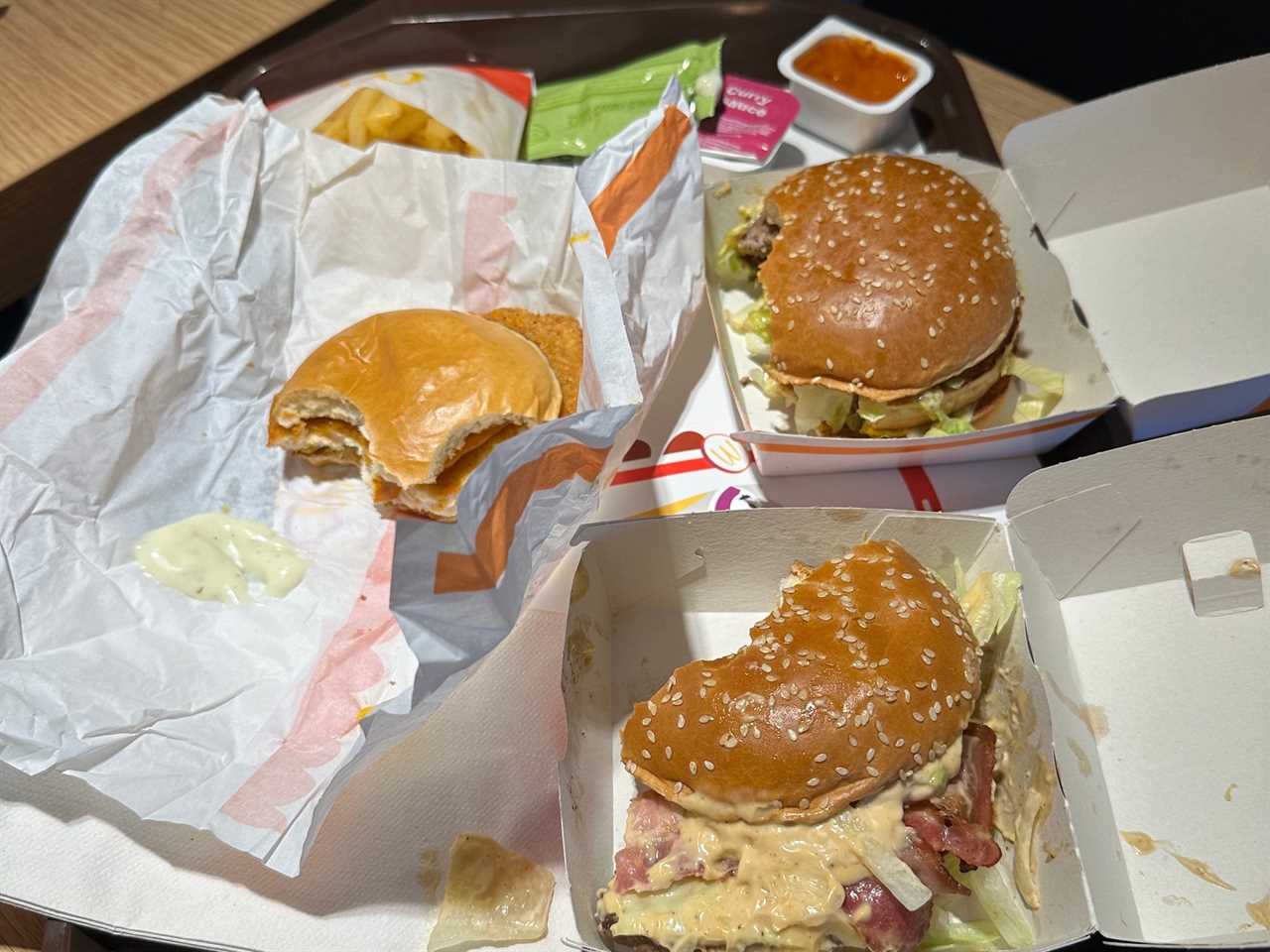 mcdonalds order on a tray on a wood table with three half-eaten sandwiches, receipt, fries, and dipping sauce containers