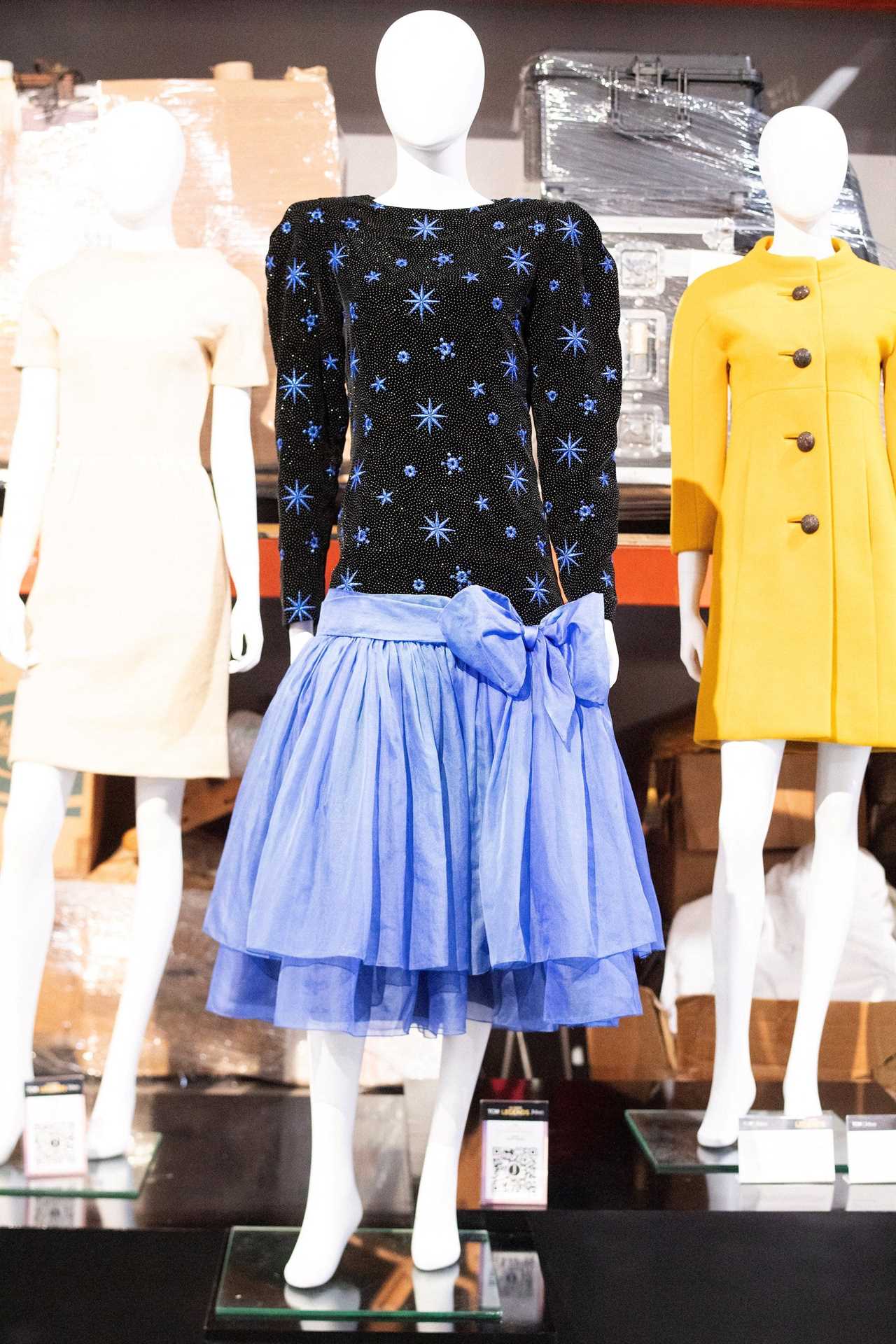 A blue and black dress sits on a mannequin next to a white and yellow dress.