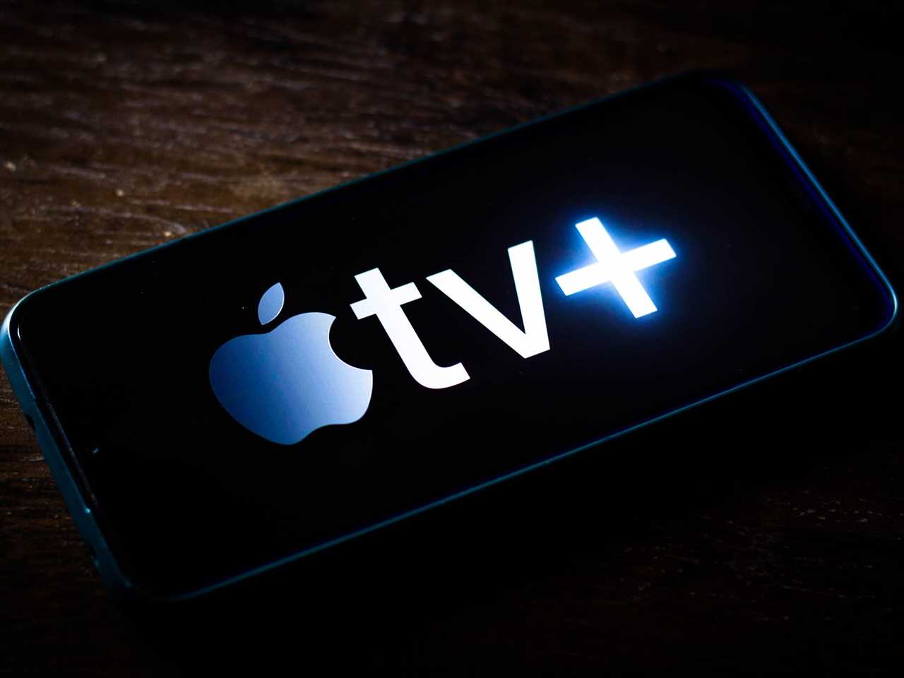 The Apple TV Plus logo displayed on a smartphone resting on a table.