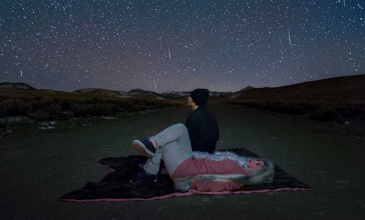 Yound adults look up at the sky, wearing heavy winter clothes and laying on a blanket.