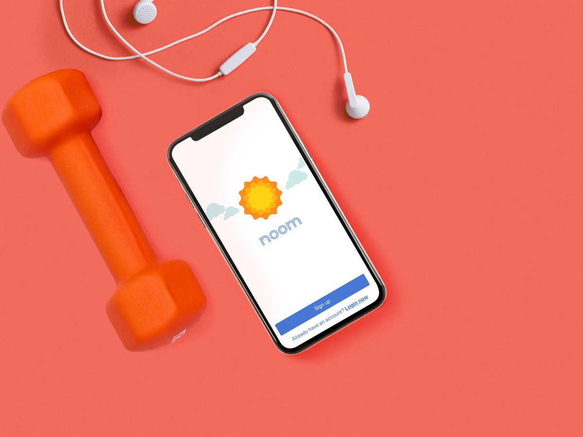 Dumbbell next to a set of wired headphones and a smartphone with the Noom app on the screen.