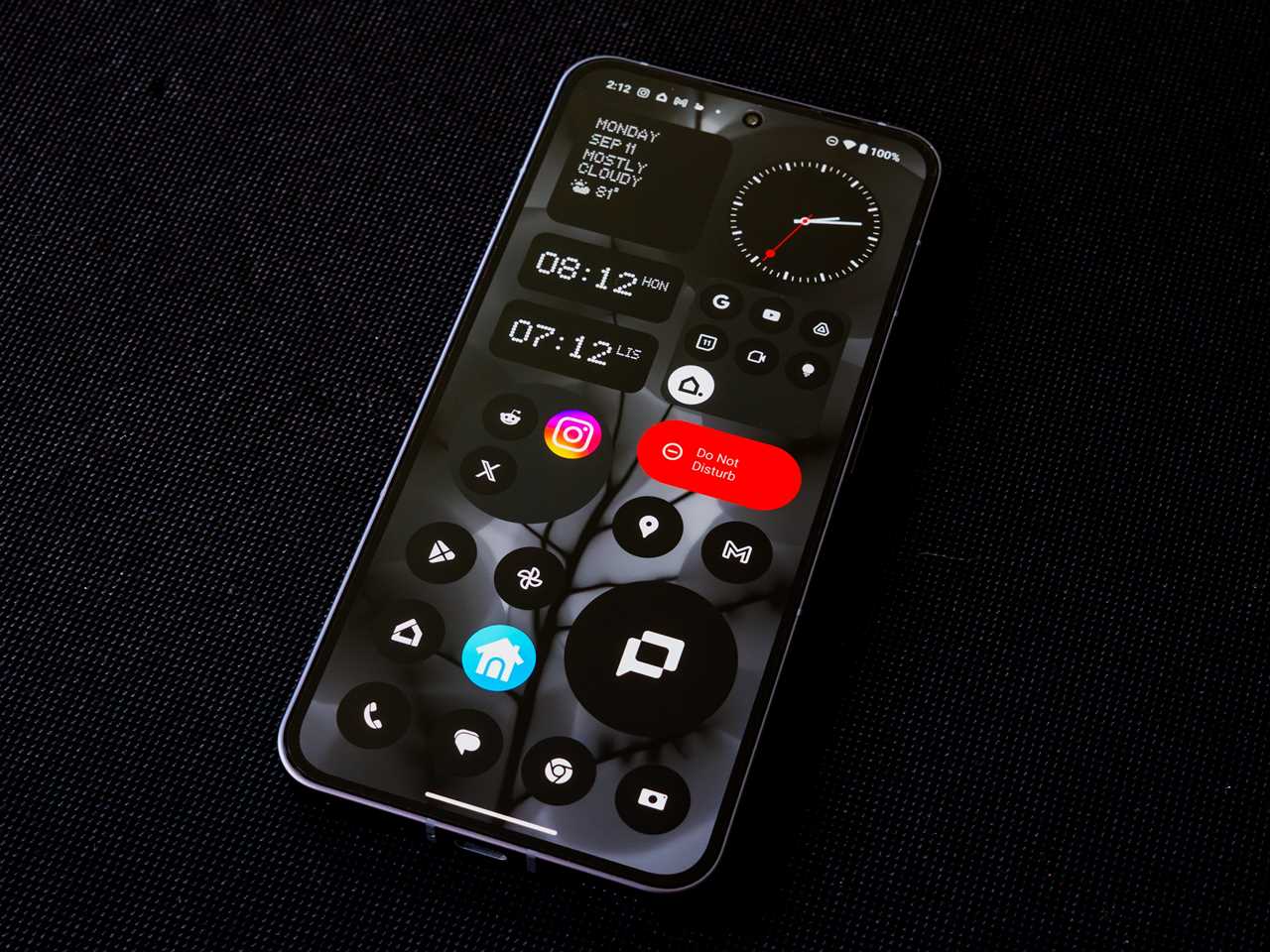 The Nothing Phone 2 against a black fabric background with the home screen showing app icons and widgets.