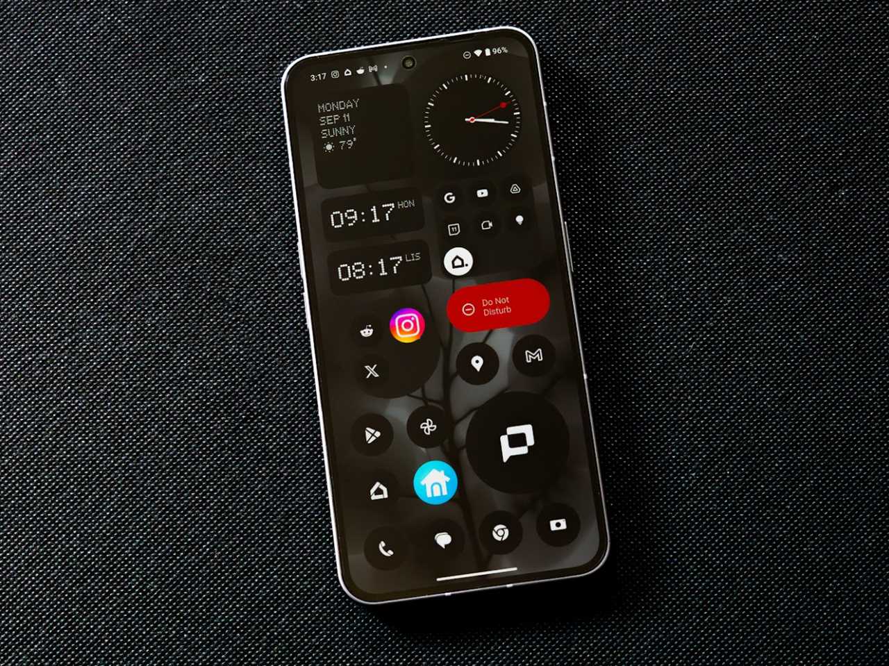 The Nothing Phone 2 with the home screen showing app icons and widgets against a black fabric background.