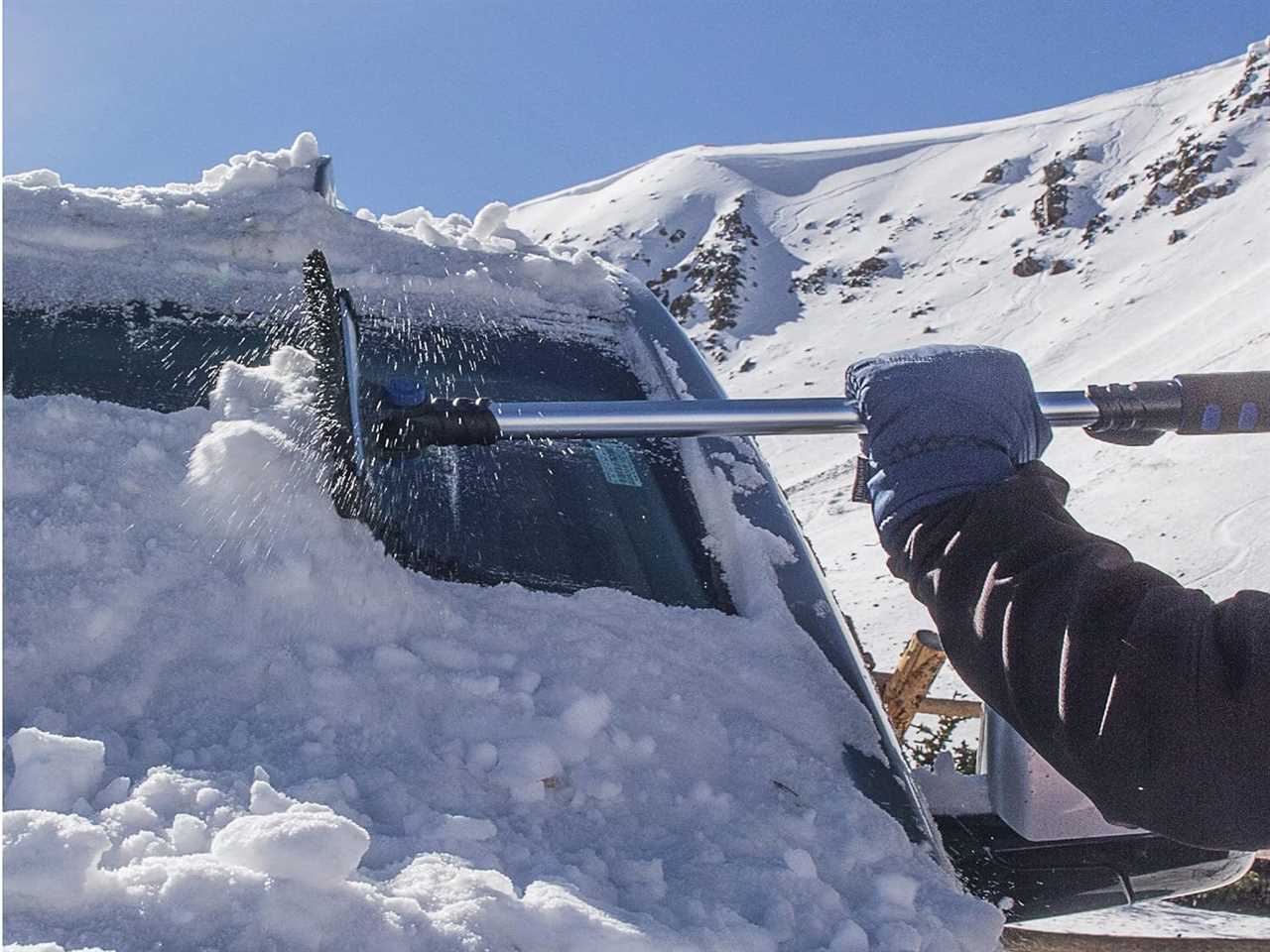 A gloved hand cleaning off a snow-covered car with the Hopkins Sub Zero ice scraper.