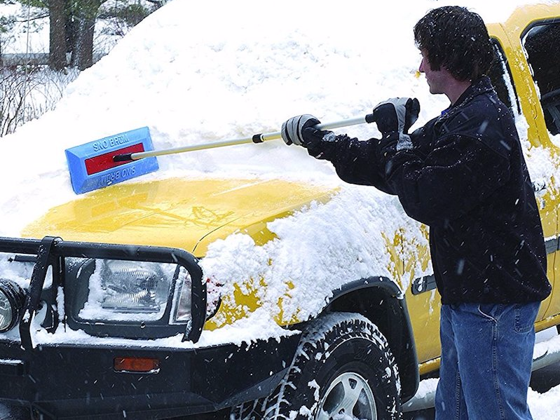 A person using an auto SnoBrum to brush snow off their vehicle.