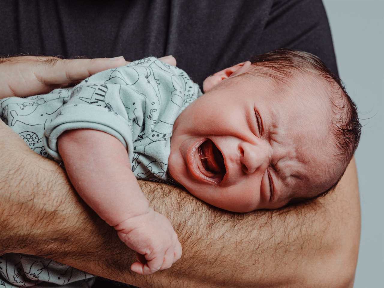 Newborn on his father's arm screams crying with expression of suffering - stock photo