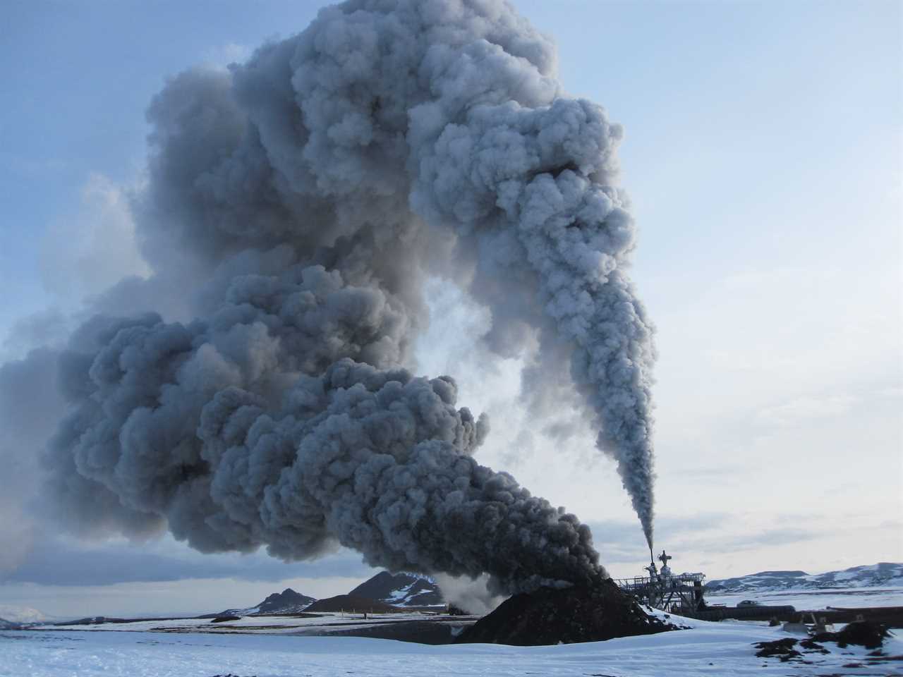 A picture shows clouds billowing out of the a rig and of a hole in the ground, on a snowy backdrop.