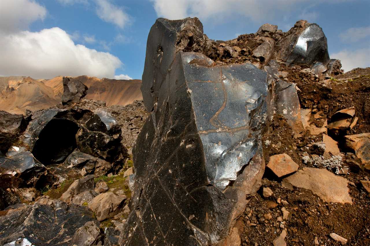 a picture shows Obsidian, a glassy rock, shown buried in the ground.