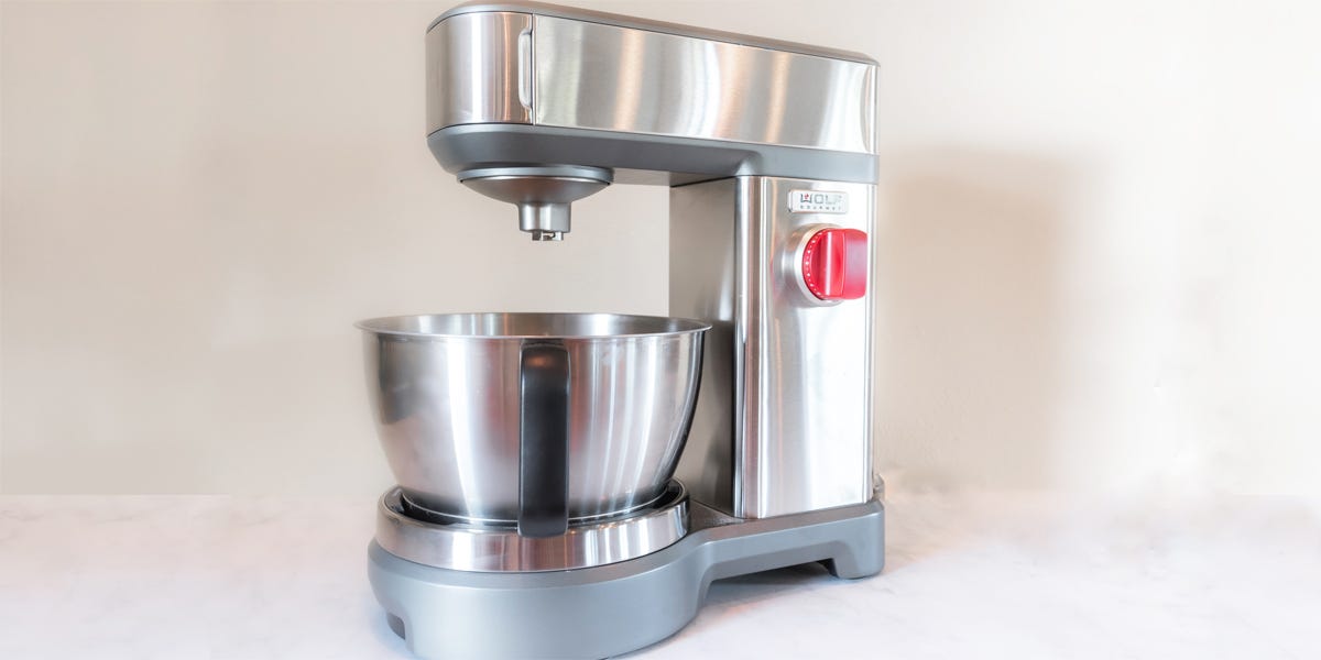 A stainless steel Wolf Gourmet Stand Mixer on a white countertop.