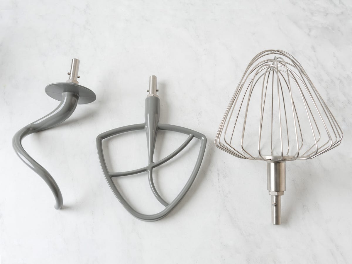 A dough hook, flat beater, and triangular balloon whisk from the Wolf Gourmet Stand Mixer on a marble counter.