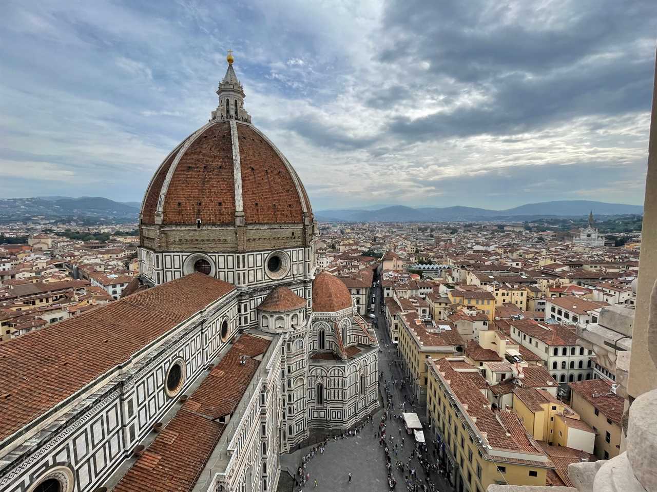 A church with brown roofing and white, detailed siding stands tall next to smaller houses in Florence, Italy