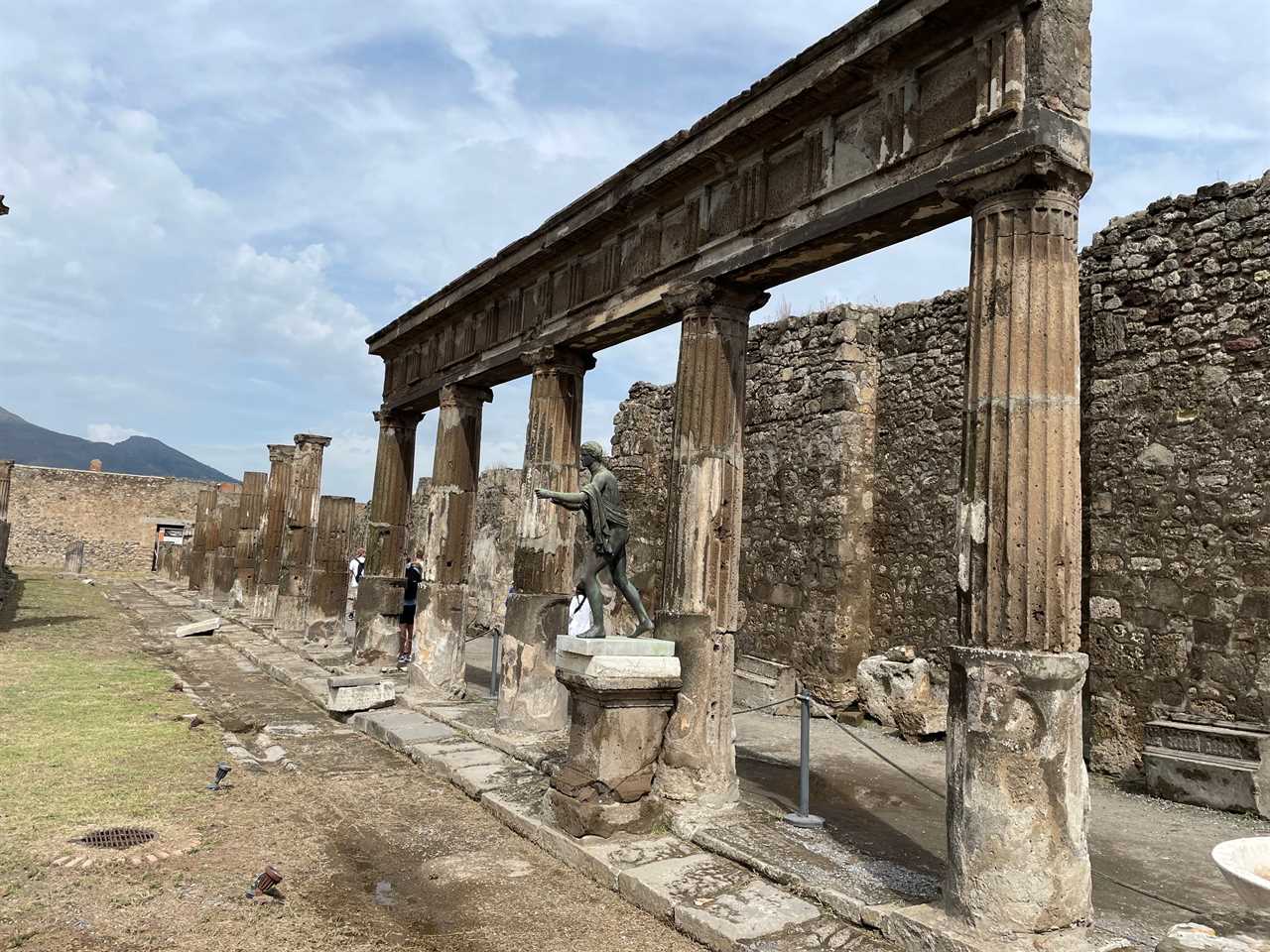 A brick wall, several columns, and a statue of a man among ruins in Pompeii