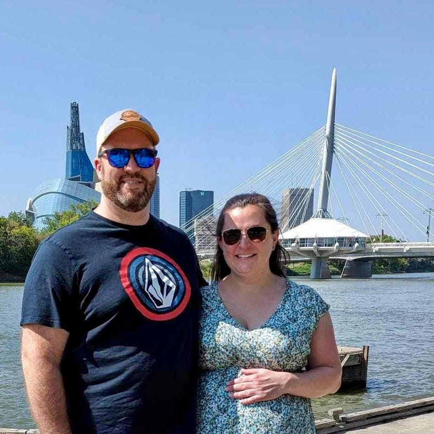 A man and a woman posing in front of water and a bridge.