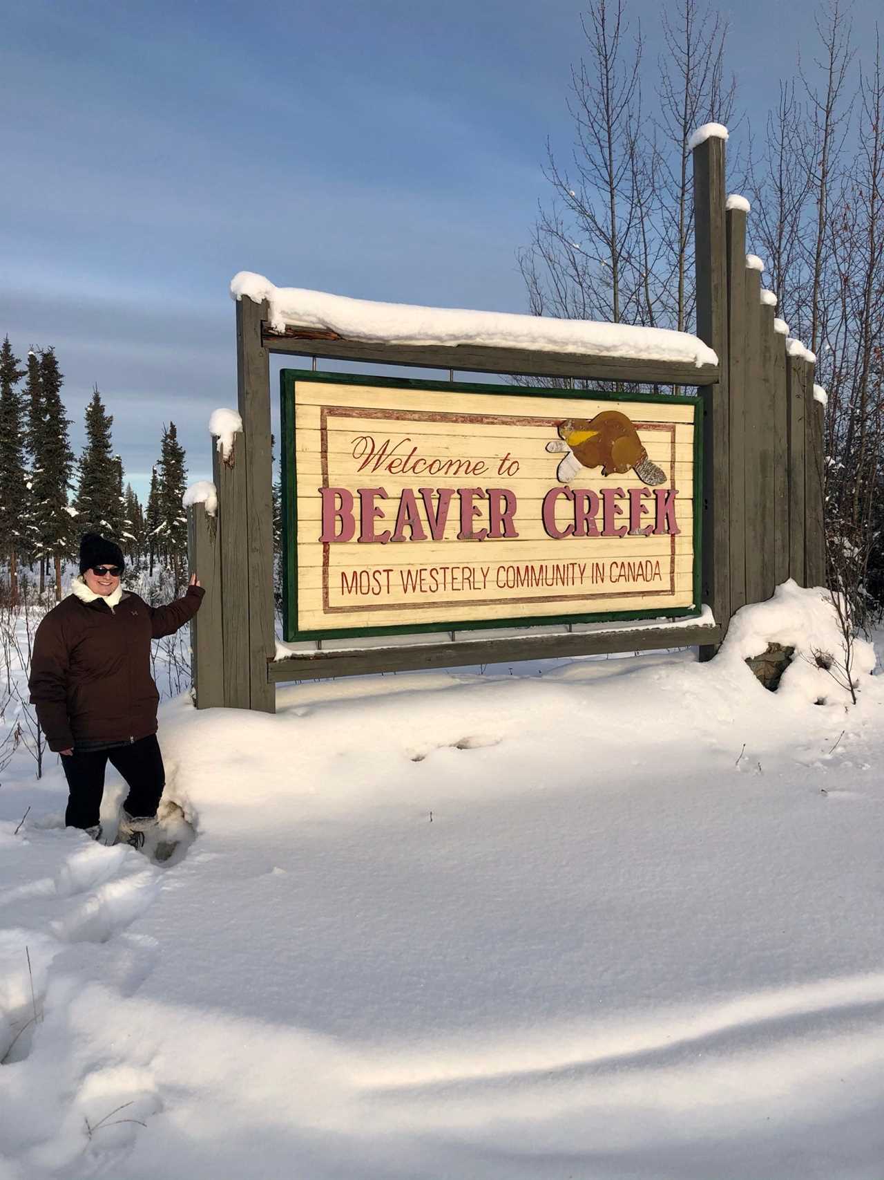 A woman posing in knee-high snow in front of a sign in Canada.