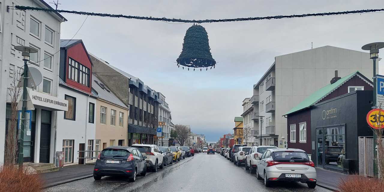 The view down a street in Iceland, showing buildings, cars, and mountains and the sea in the distance