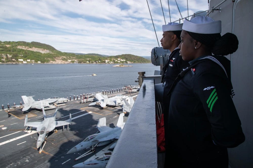 sailors aboard a military aircraft carrier man the rails