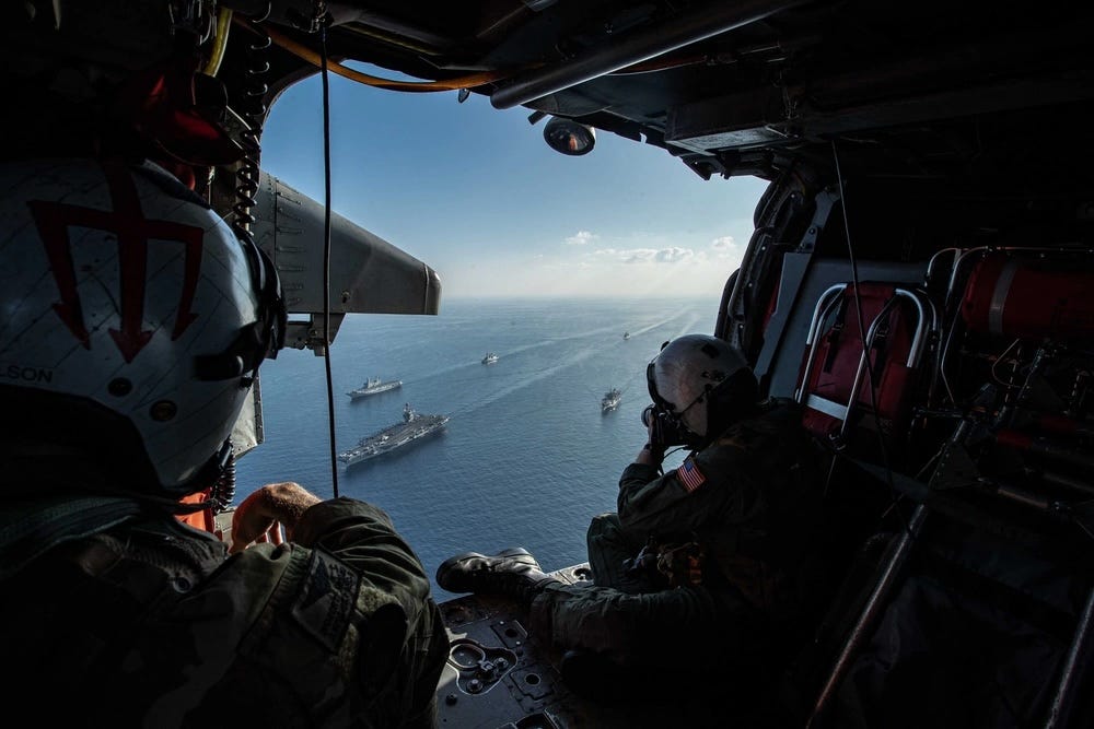 a photographer aboard a helicopter takes photos of a fleet of military ship from the sky