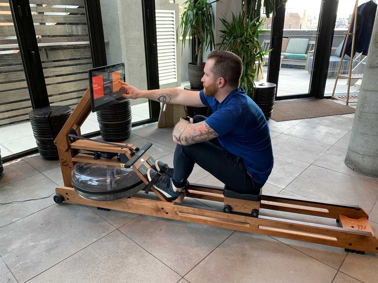 the author touches the screen of the Ergatta Connected Rower in a living space.