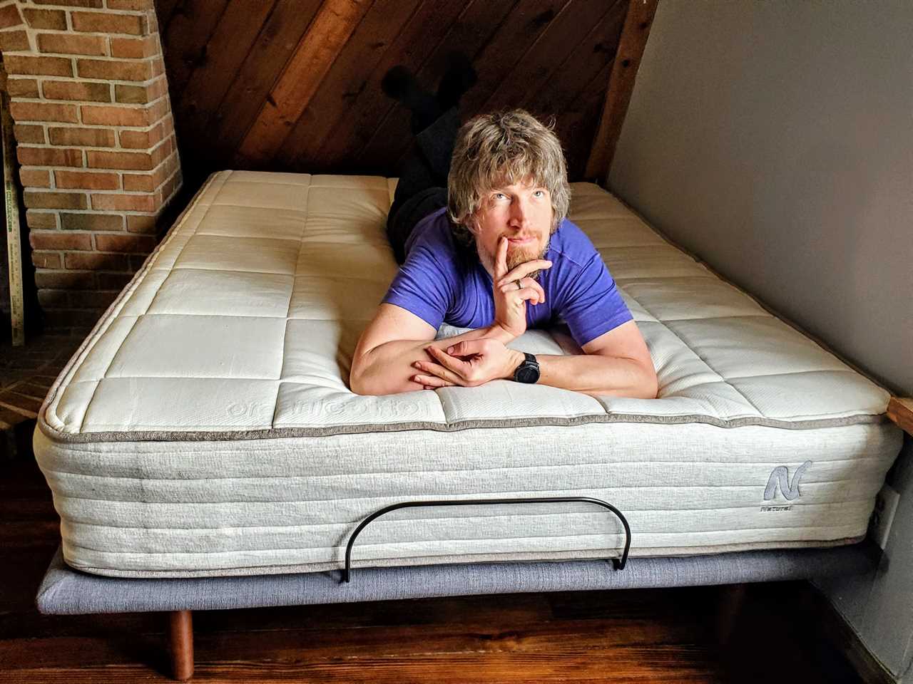 Author James Brains laying on the 11 inch nolah natural mattress set atop a bed frame.