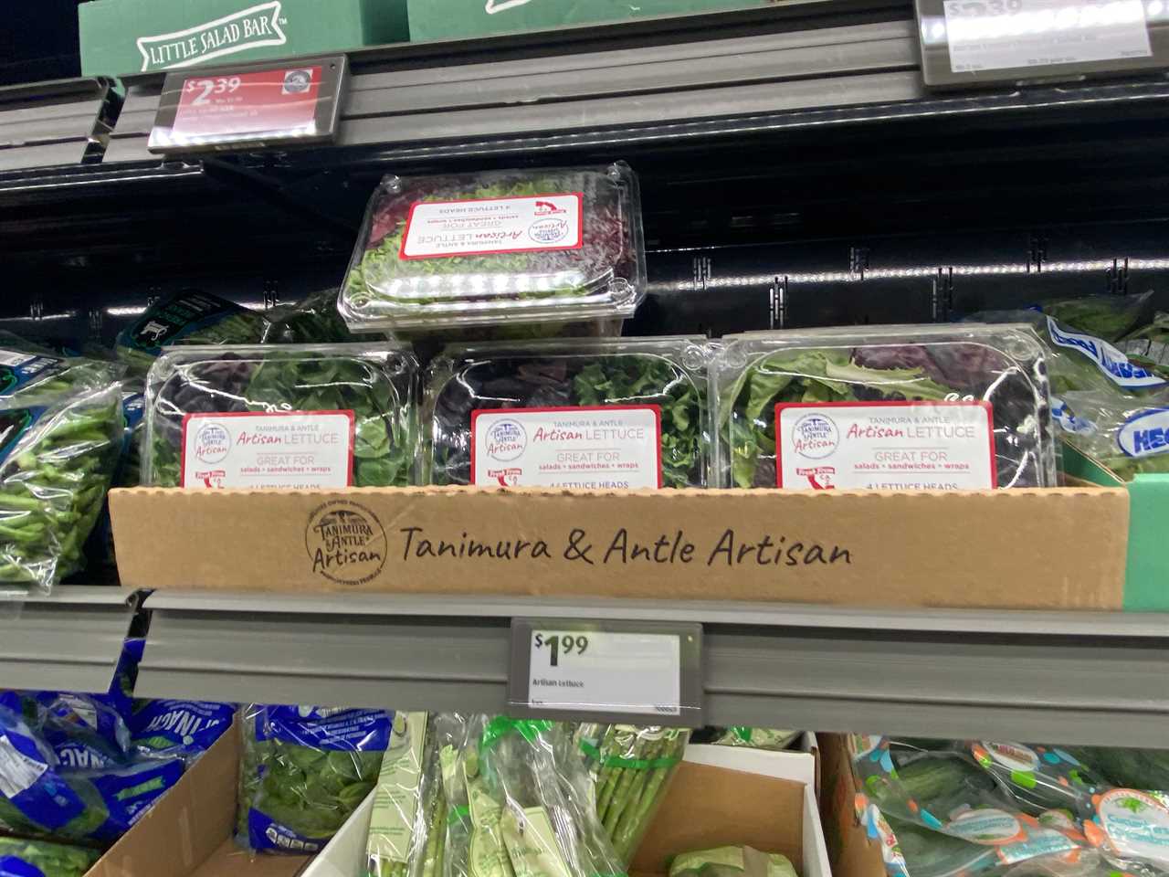 Four clear plastic packages of Tanimura artisan lettuce on shelves at Aldi