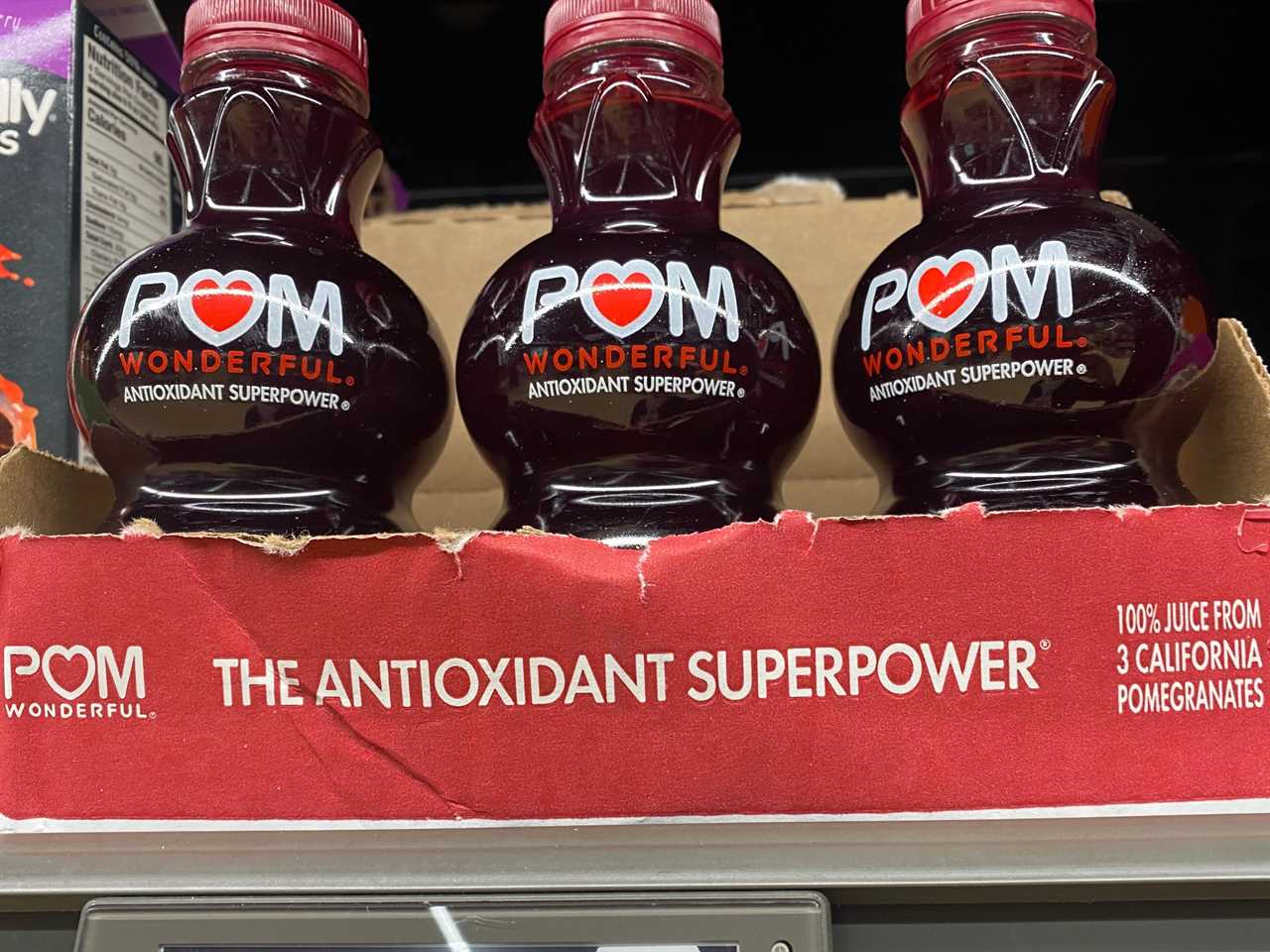 Red box of three clear bottles of deep-red POM juice