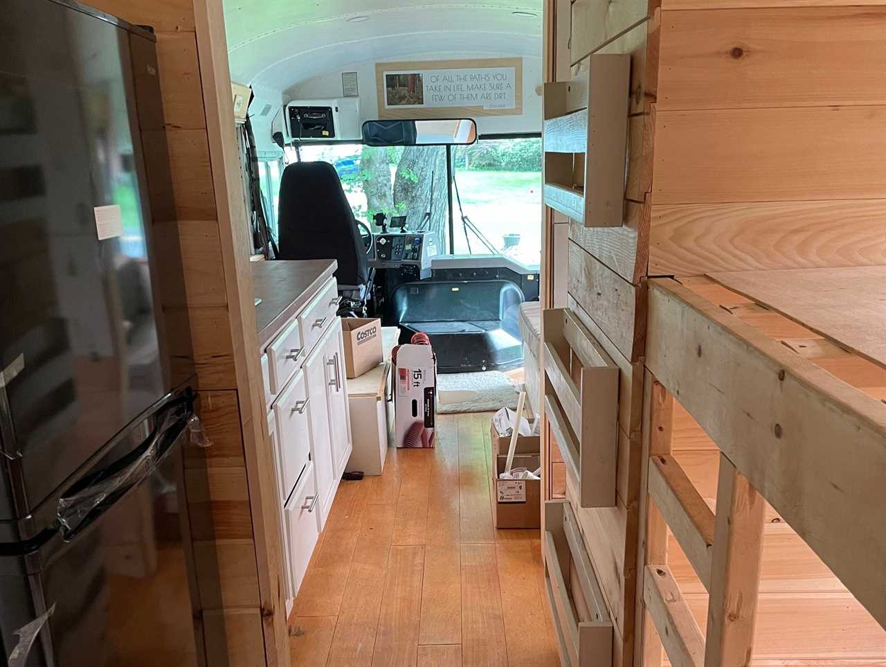 Wooden shelves and drawers and black refrigerator with view of white cabinets and driver's area in front of businside redesigned school bus