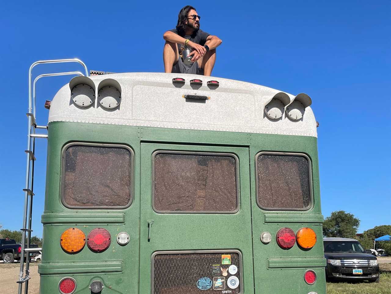 Man sits on top of green school bus with built-on ladder on left side of bus