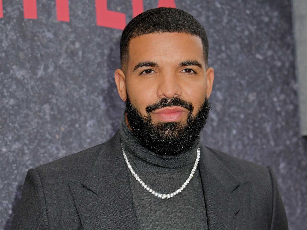 Drake, wearing a black sports coat and a pearl necklace, poses on the red carpet.