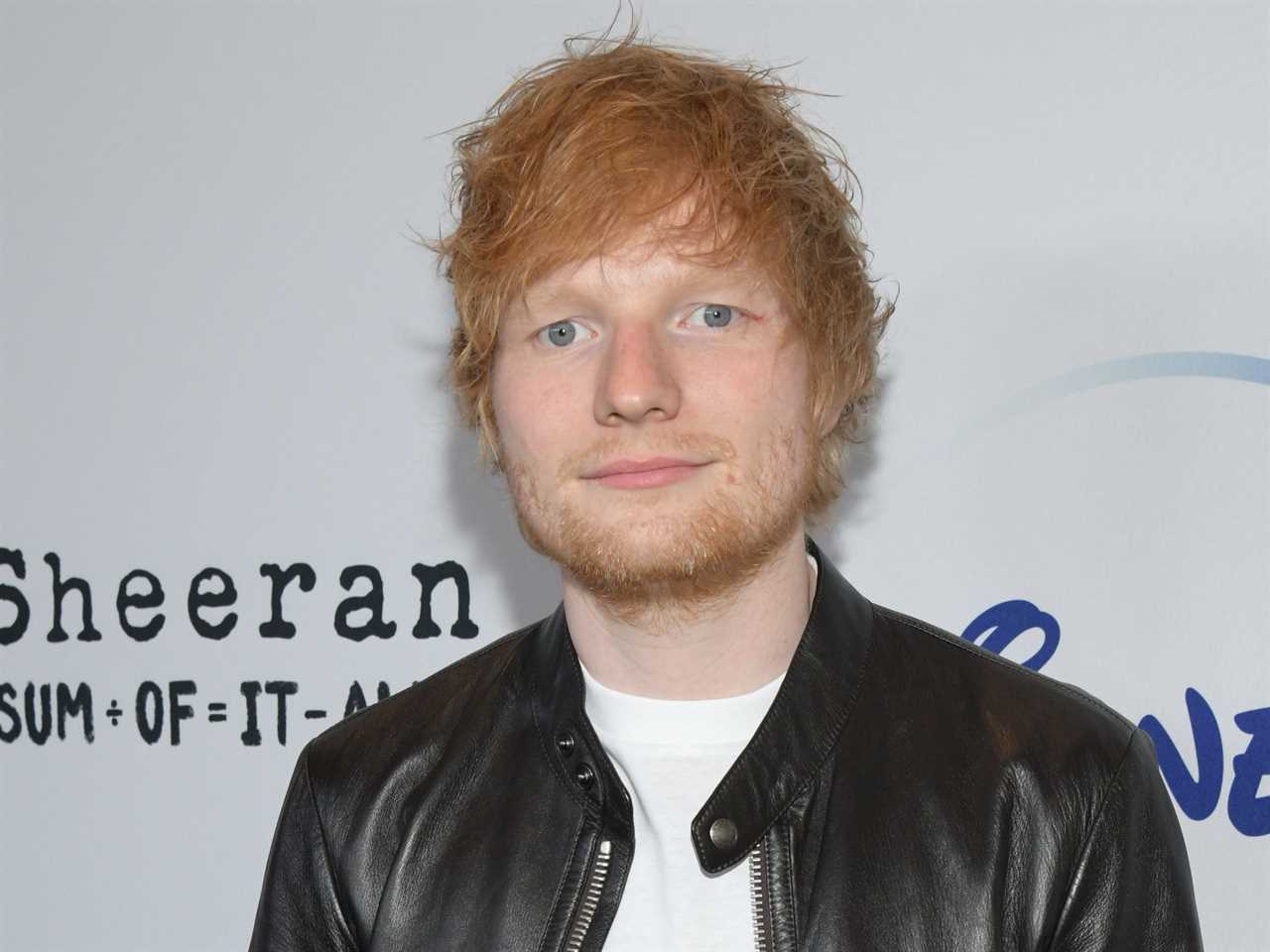 Ed Sheeran wears a white t-shirt and  leather jacket on the red carpet premiere of his movie "The Sum of it All."