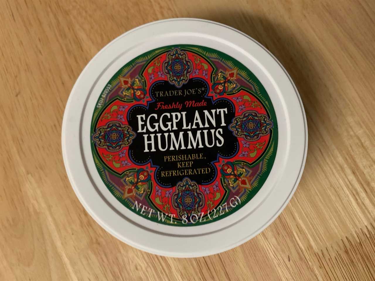 red and white container of trader joe's eggplant hummus on wood table