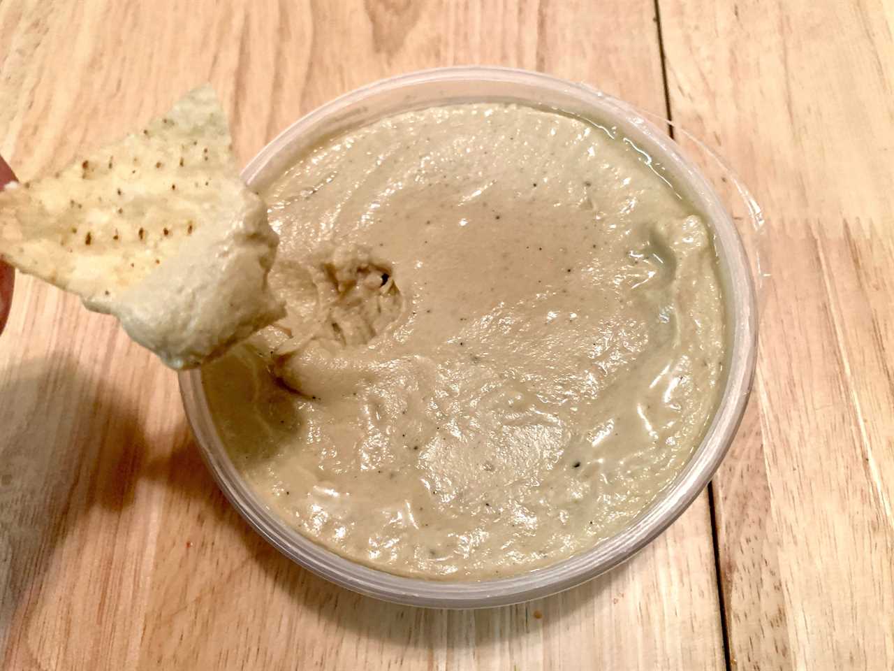 hand dipping chip into trader joe's eggplant hummus