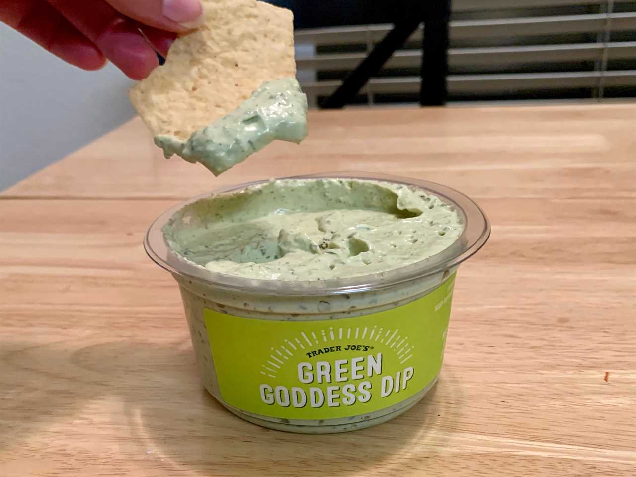 chipping dipping in green tub of trader joe's green goddess dip