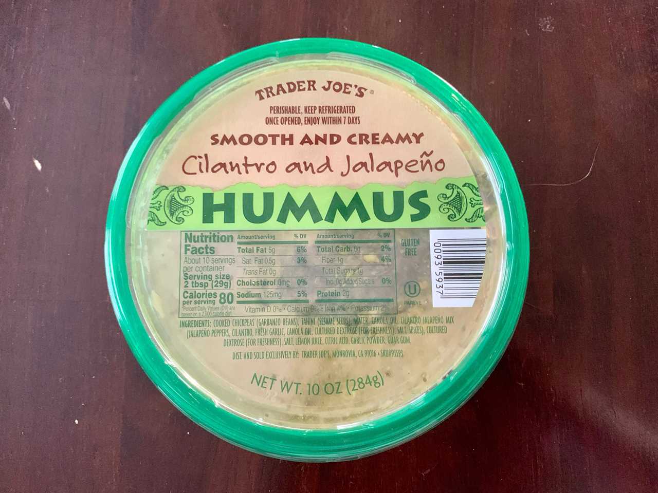 green and beige tub of trader joe's cilantro jalepeno hummus on wood table