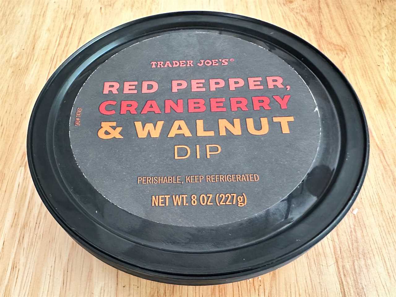 Black container of Trader Joe's red pepper, cranberry, and walnut dip on light wood table