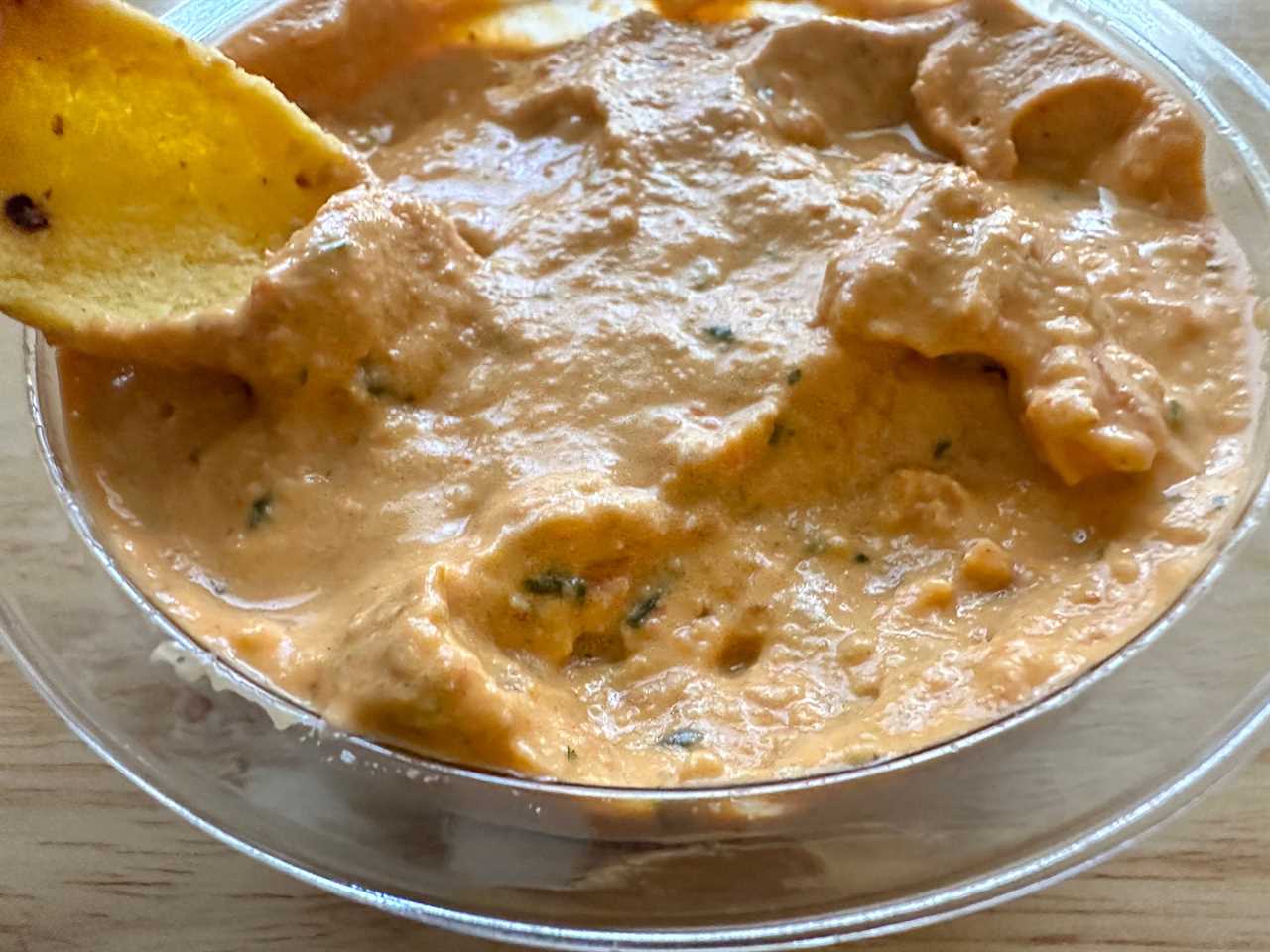 A corn chip dipping into Trader Joe's vegan Buffalo dip