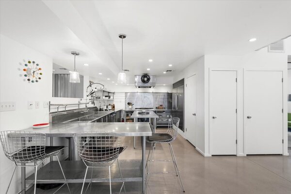 Steps from the main entrance is a spacious, industrial-like kitchen, complete with long stainless-steel countertops and open shelving.